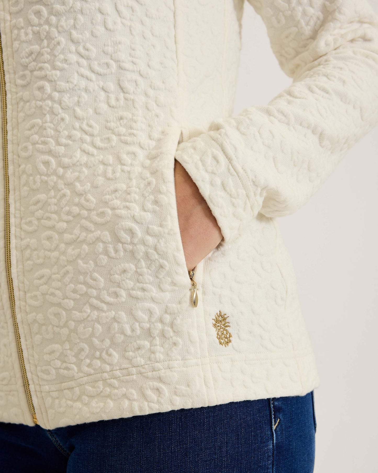 Hannahs Of Erin- Erin Ontario-Tommy Bahama -Aruba Sweatshirt- Style # SW222047  colour coconut(off white) featuring a zip-up design, mock neckline, and zippered pockets, adorned with a jacquard animal print. Made from a blend of 63% cotton, 35% recycled polyester, and 2% spandex, this sweatshirt offers a touch of stretch for comfort. An eco-friendly and stylish choice, perfect for all-day wear.